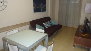 A living room with a dining table, chairs, a sofa, a clock, and a painting of a cityscape. - P. Maritimo 3º Pta 13 * LEK (Peñiscola)