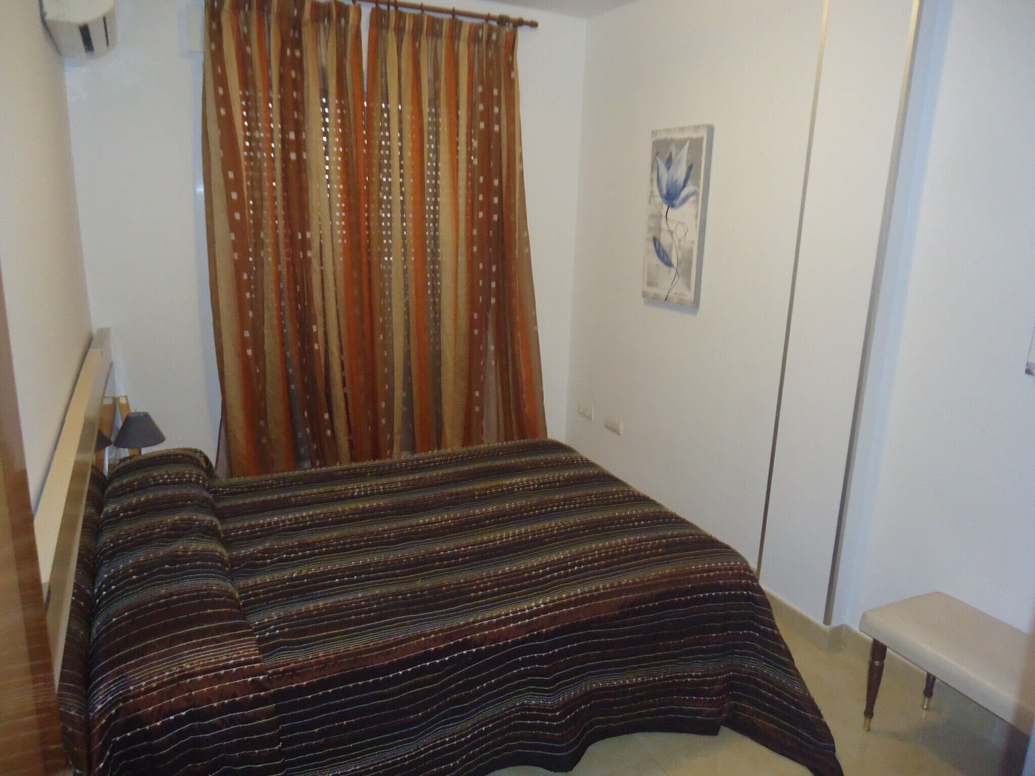 A bedroom with a bed, a bench, a curtain, and a wall-mounted light fixture.