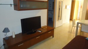 A modern living room with a flat-screen TV on a wooden cabinet, a small table with a candle, and a mirror on the wall. - P. Maritimo 3º Pta 13 * LEK (Peñiscola)