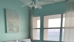 A bedroom with a bed, a nightstand, a ceiling fan, a window with curtains, and a painting on the wall. - Oceanfront Beachfront Penthouse, Isla Verde (Carolina)