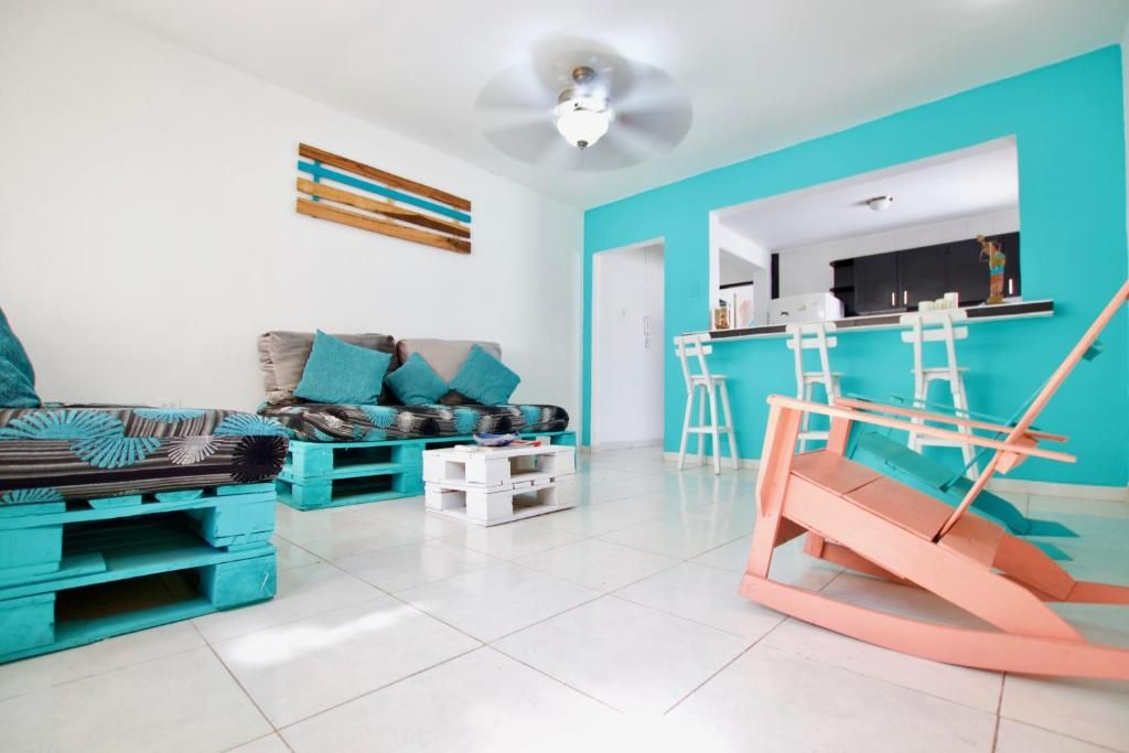 Een moderne woonkamer met een blauwgroene accentmuur, een bank met decoratieve kussens, een salontafel en een bijzondere houten constructie die lijkt op een schommel.