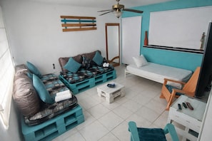 A compact living space with a sofa, a small table, a chair, and a ceiling fan. - QuillaHost Thematic Apartment (Barranquilla)