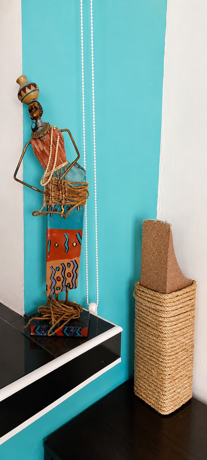 A decorative sculpture with a woven base, a woven basket, and a white wall with teal and white panels.