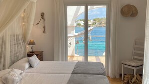 A bedroom with two beds, a ceiling fan, a nightstand with a lamp, and a view of a pool and buildings. - House / Villa - Portocolom (Portocolom)