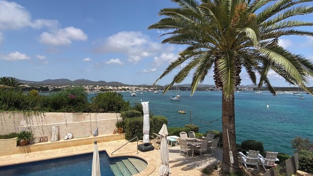 A poolside area with lounge chairs, a palm tree, and a view of the sea with boats. - House / Villa - Portocolom (Portocolom)