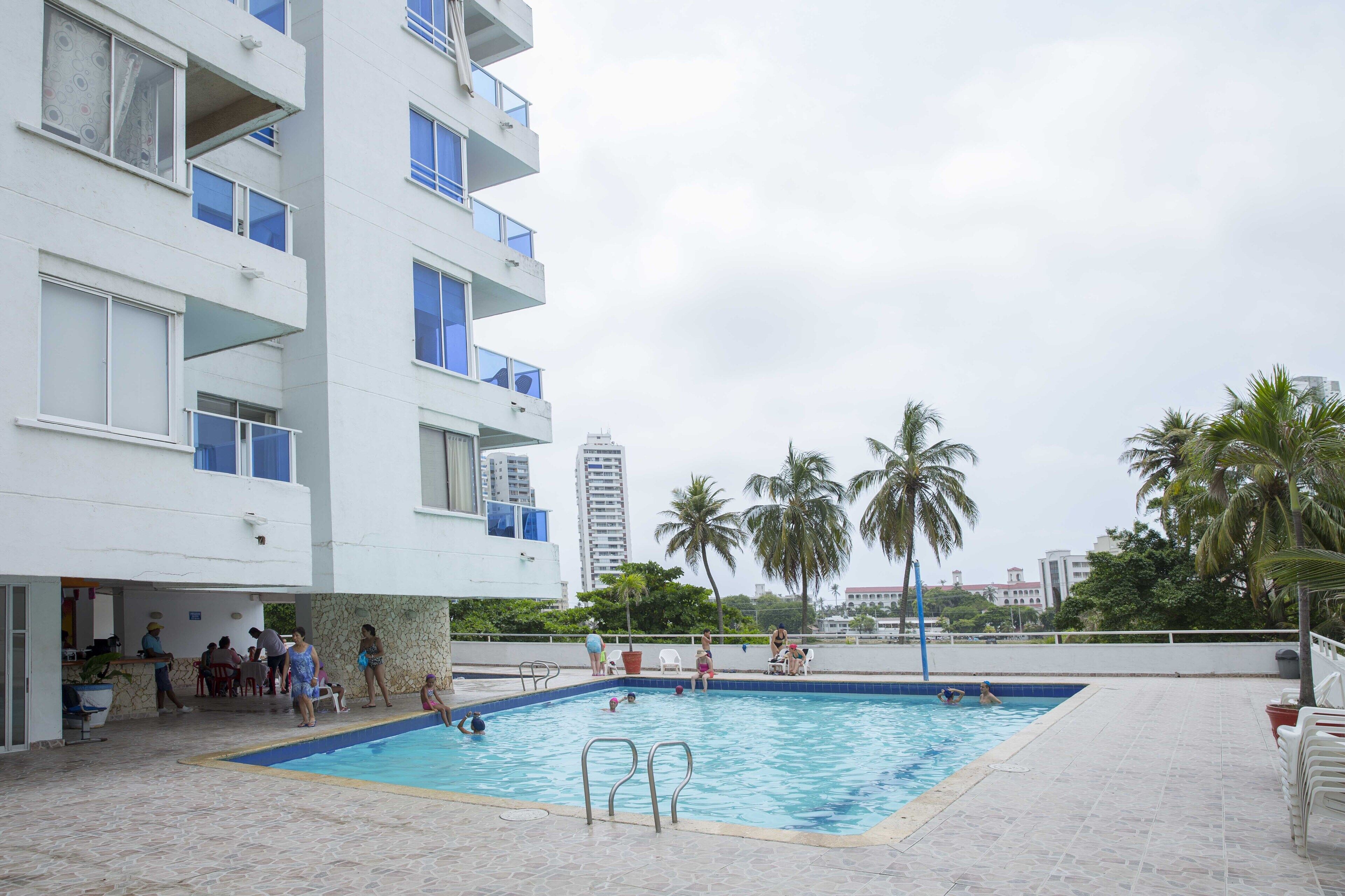 A swimming pool area with a building, palm trees, and a view of a tall building in the background.