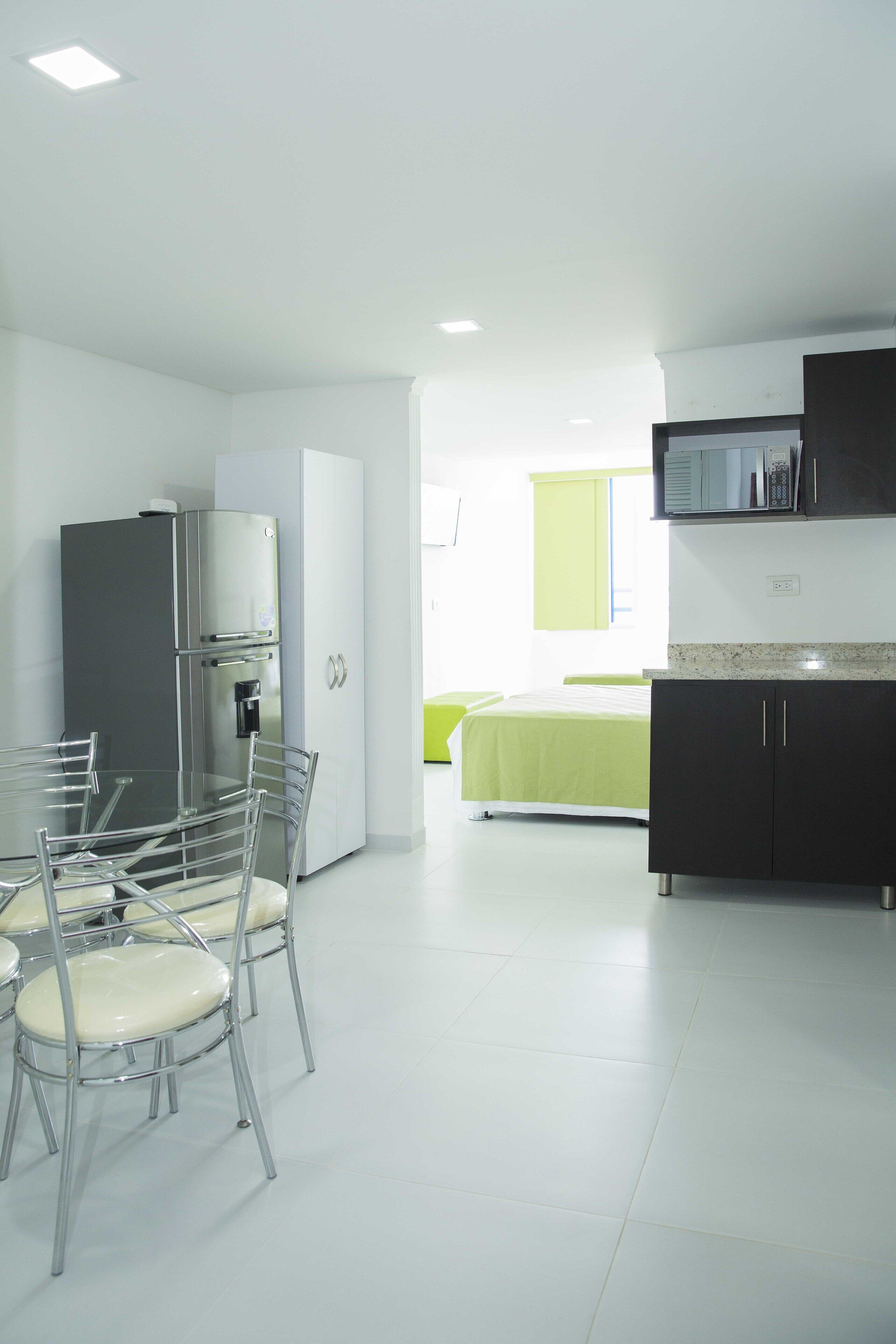 A modern kitchen with a refrigerator, microwave, and cabinets. There is a dining area with a table and chairs.