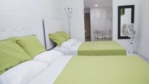 Een hotelkamer met twee bedden, elk met groen-witte beddengoed. Er staat een ventilator aan de muur en er is een stoel op de achtergrond.