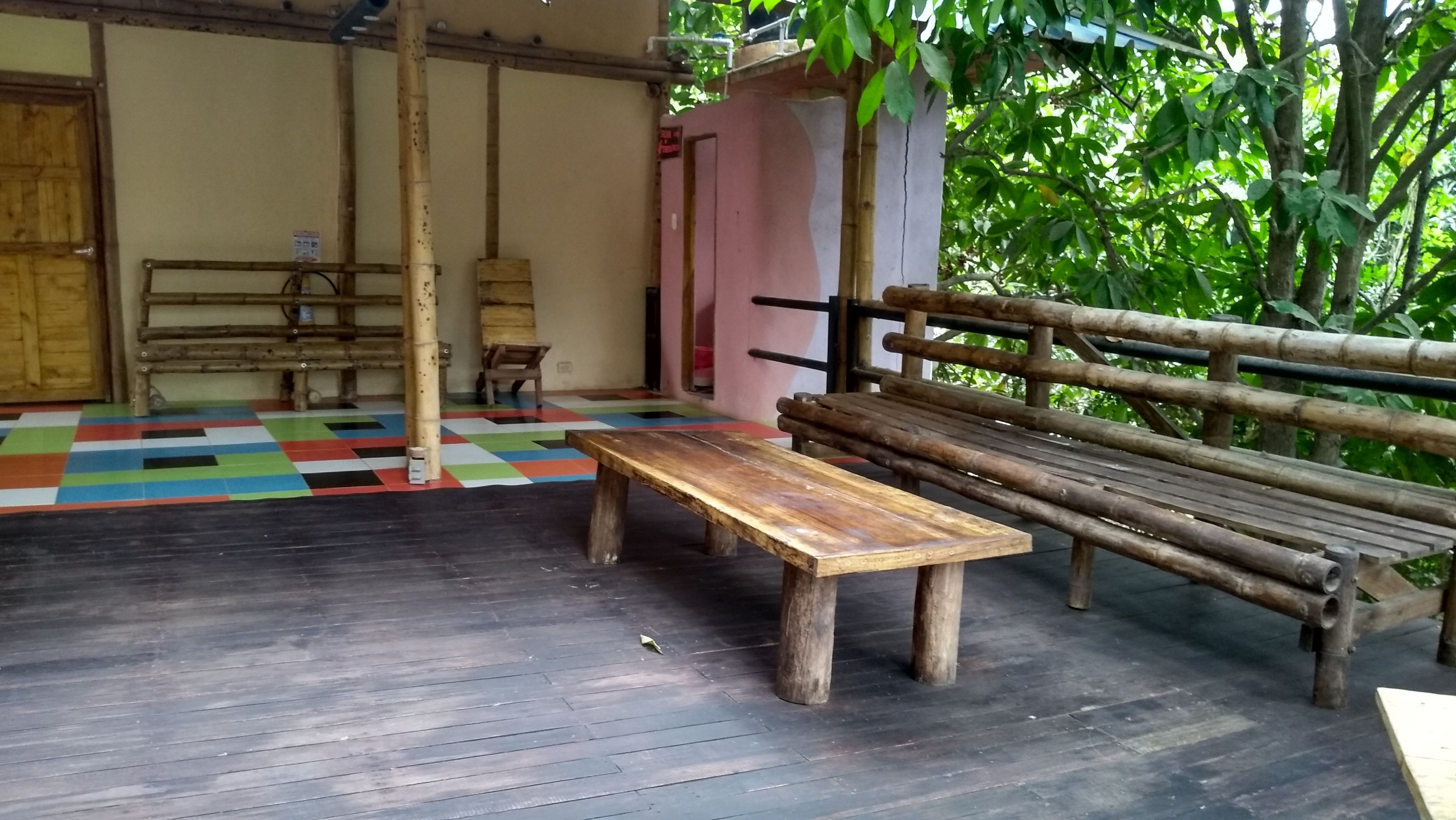 A wooden bench and table in a room with a colorful floor, a bamboo railing, and a door in the background.