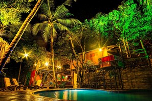 A nighttime view of a pool area with lounge chairs, a pool, and a building with a staircase. - Kanta Sana (Dibulla)