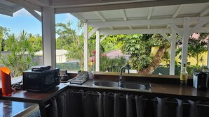 A kitchen with a view of a lush garden, a microwave, a sink, and a kettle. - Bungalow F2 deluxe in beautiful Art Deco property and tropical garden (Petit Bourg)