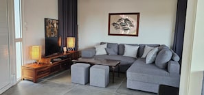 Un salón moderno con un sofá gris, otomanas, una mesa de centro de madera, un televisor y una lámpara de pie.