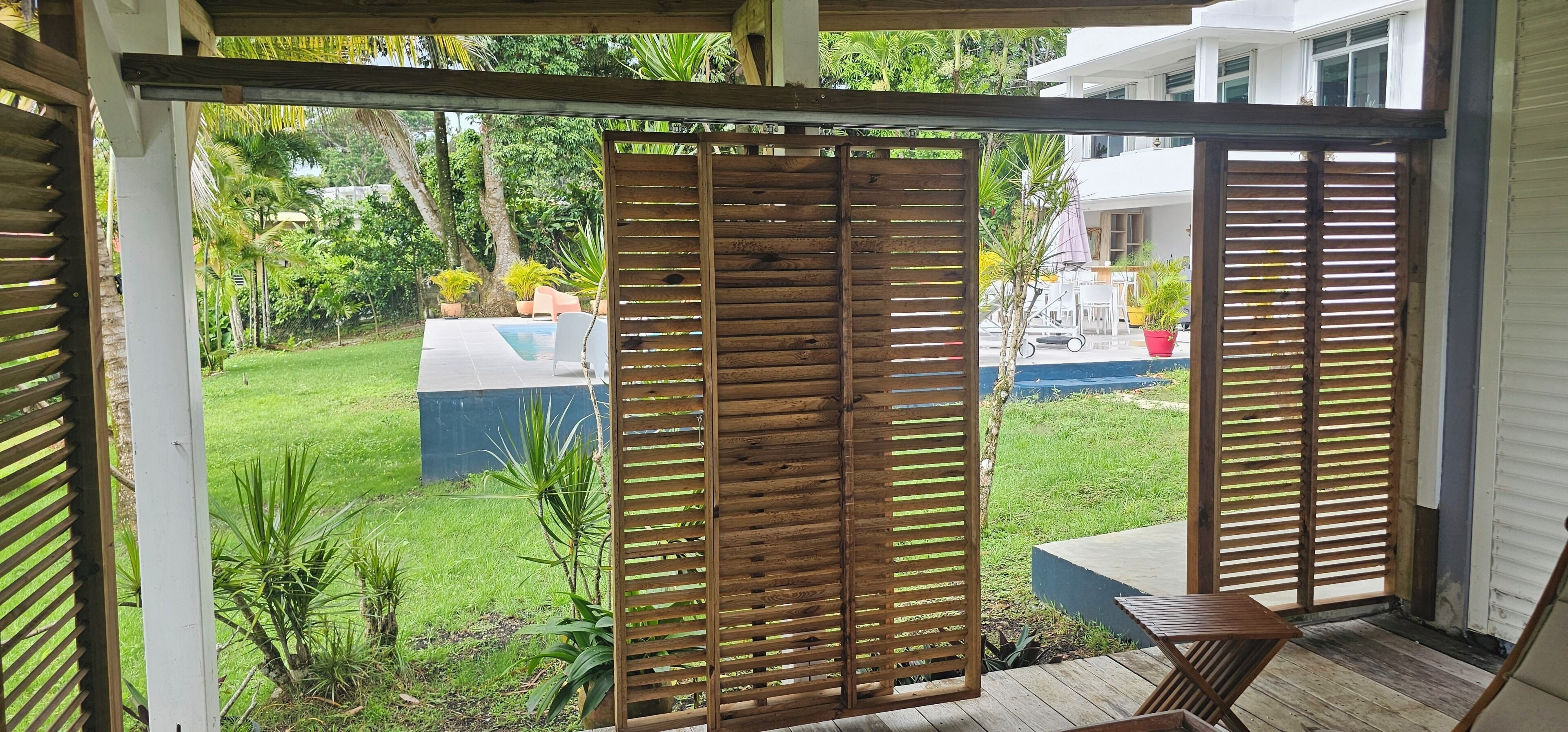 A covered outdoor area with a wooden fence, a pool, and a view of a house in the background.
