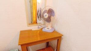Un escritorio de madera con un ventilador de pie, un espejo y un taburete pequeño.