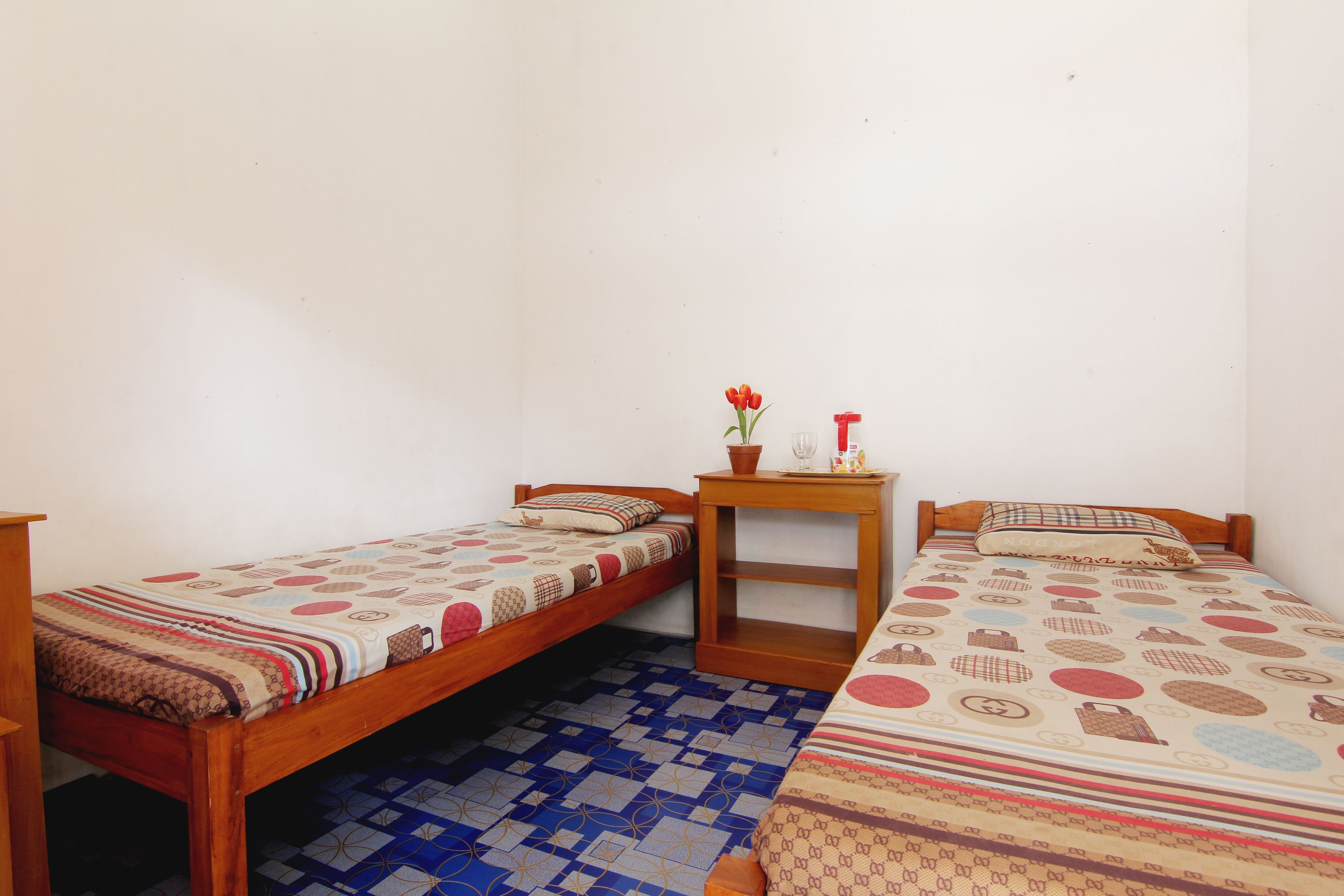 A small room with two wooden beds, a small table with a vase of flowers, and a patterned blue and white floor.