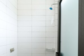 A shower area with white tiled walls and a metal showerhead. - Riviera Residence (Balikpapan)