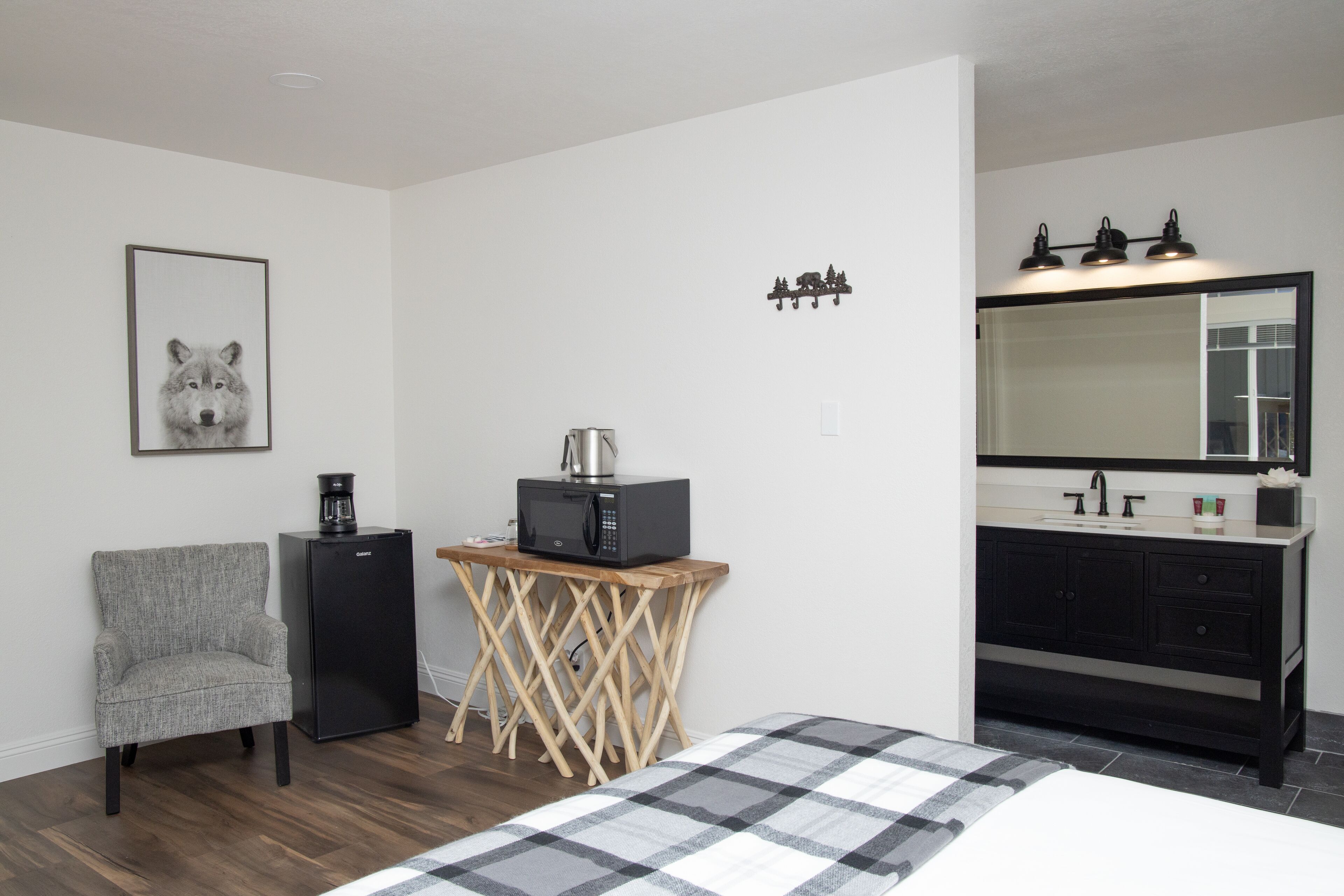 A bedroom with a bed, a chair, a small table with a microwave, a coffee maker, a sink, and a mirror.