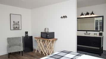 A bedroom with a bed, a chair, a small table with a microwave, a coffee maker, a sink, and a mirror.