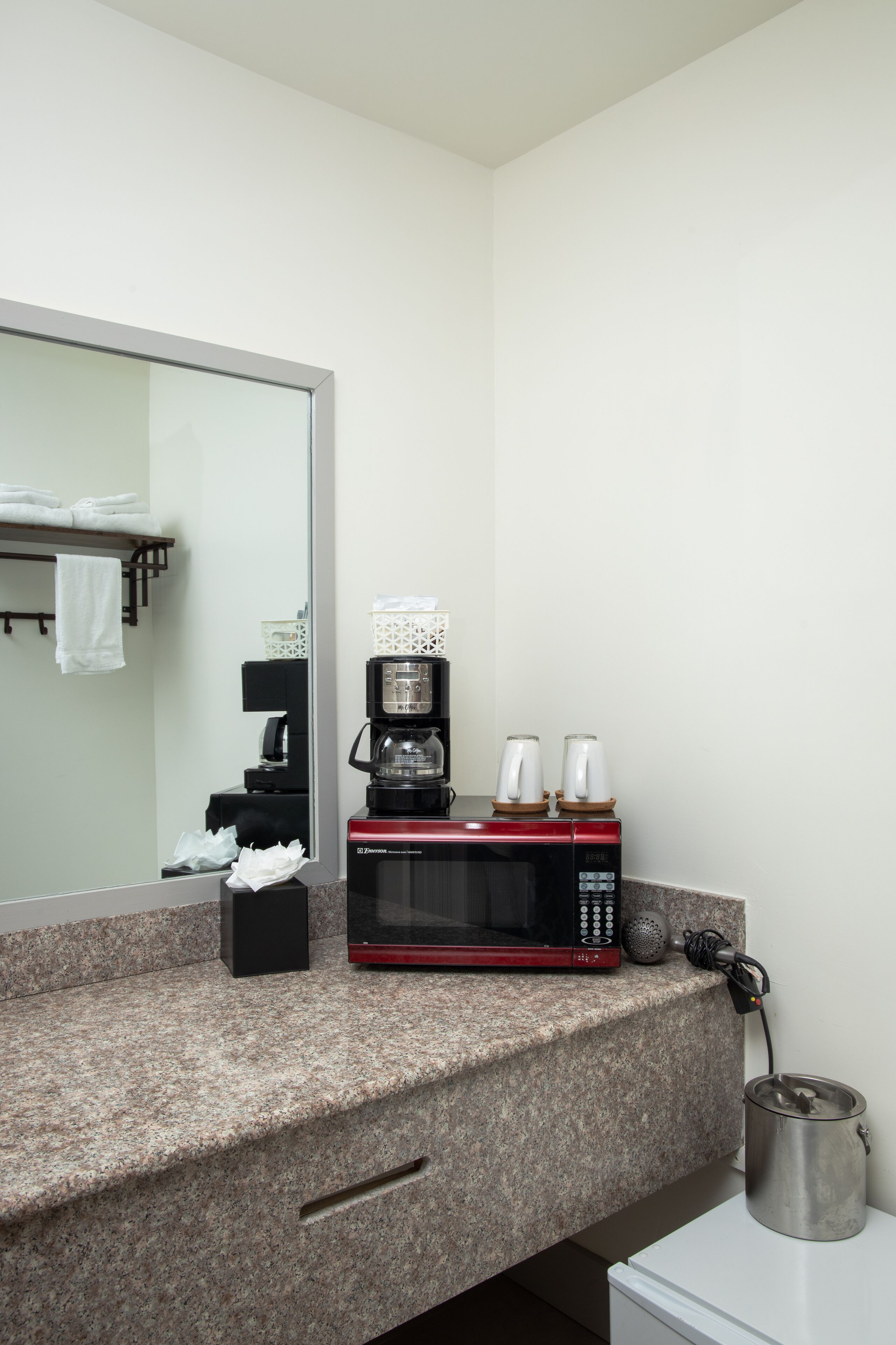 Une salle de bain moderne avec un comptoir en granit, une machine à café noire et rouge, un four à micro-ondes et une petite poubelle.