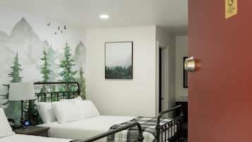 Habitación de hotel con dos camas, un mural de montañas, un cuadro enmarcado y una puerta con un cartel de número.