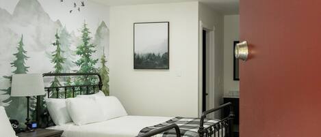A hotel room with two beds, a mountain mural, a framed picture, and a door with a number sign.