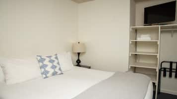 A hotel room with a bed, a TV on a stand, a lamp, and a closet with shelves.