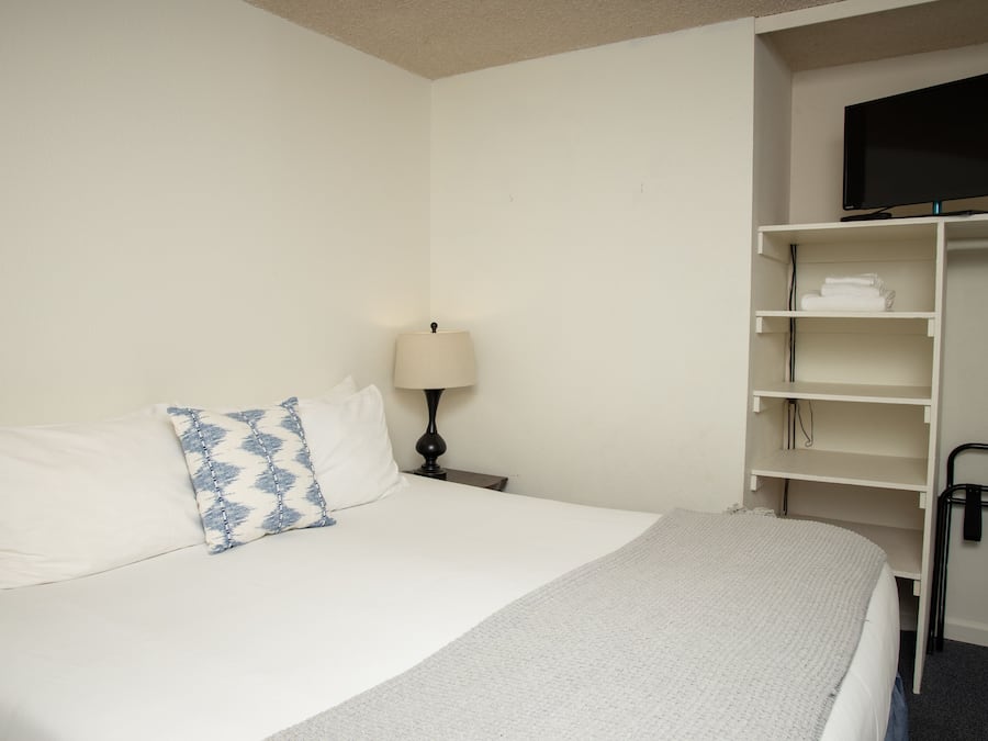 A hotel room with a bed, a TV on a stand, a lamp, and a closet with shelves.