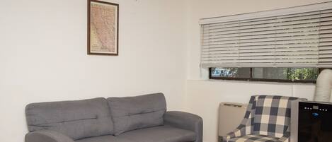 A living room with a grey sofa, a wooden coffee table, a checkered armchair, and a wall-mounted air conditioner.