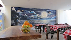 A dining area with a wooden table, a bowl of fruit, and a mural of a night scene with mountains and a moon. - Casa Luna Hotel (Santa Marta)