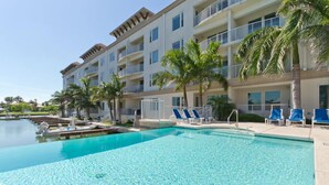 A hotel with a swimming pool, palm trees, and a multi-story building with balconies. - Las Marinas #408 | Waterfront Condo • Boat Slip • 6 Minute Walk to Beach (South Padre Island)