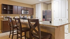 A kitchen with dark wooden cabinets, a granite countertop, a built-in microwave, a stove, a refrigerator, and two bar stools. - Las Marinas #408 | Waterfront Condo • Boat Slip • 6 Minute Walk to Beach (South Padre Island)
