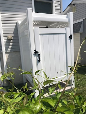 Un cobertizo exterior blanco con puerta y manija, situado en un área cubierta de césped con plantas en primer plano.