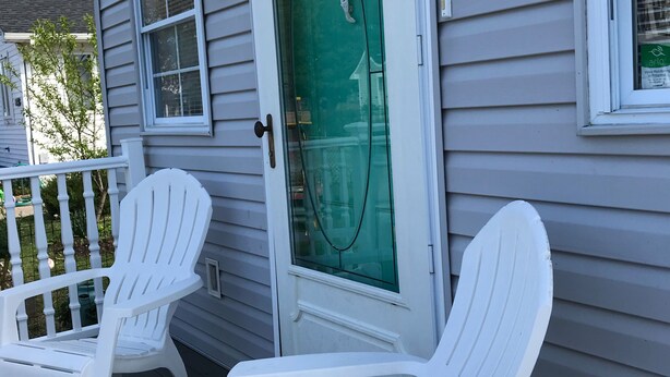 A porch with two white Adirondack chairs, a glass door with a green screen, and a white railing.