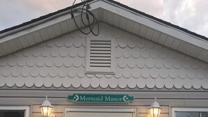 A building with a teal door, white trim, and a sign reading "Mermaid Manor".