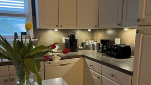 A modern kitchen with white cabinets, a marble countertop, and various appliances like a coffee maker and toaster.