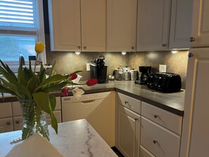 Una cocina moderna con armarios blancos, encimera de mármol y varios electrodomésticos como cafetera y tostadora.