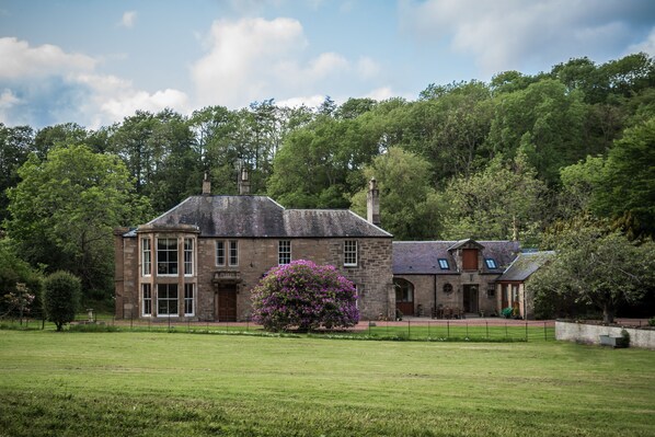 A large stone building with a central entrance, surrounded by a well-maintained lawn and a large flowering bush. - Glenarch House (Dalkeith)