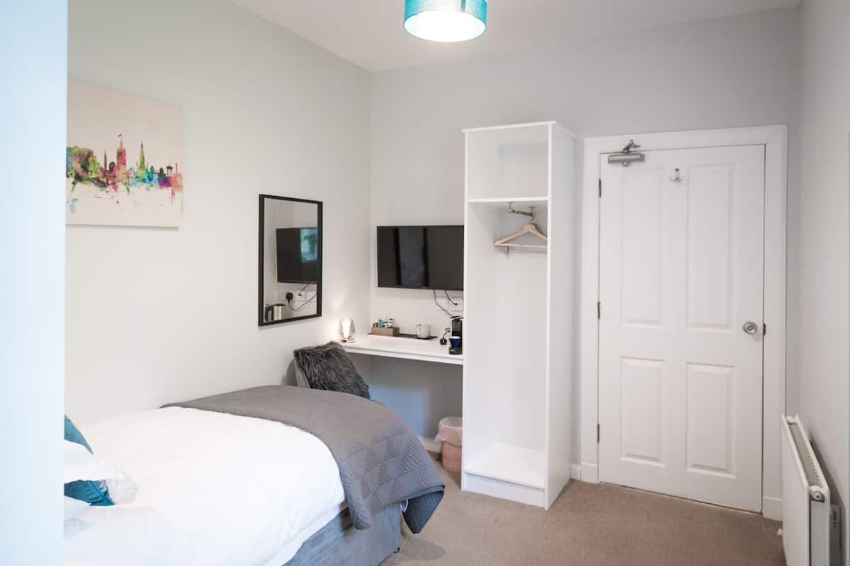 A bedroom with a bed, a desk with a computer, a TV, a wardrobe, and a door.