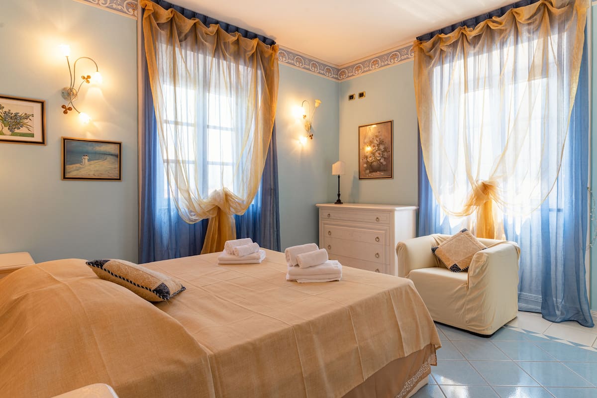 Una habitación de hotel con cama, una silla, cómoda y cortinas.
