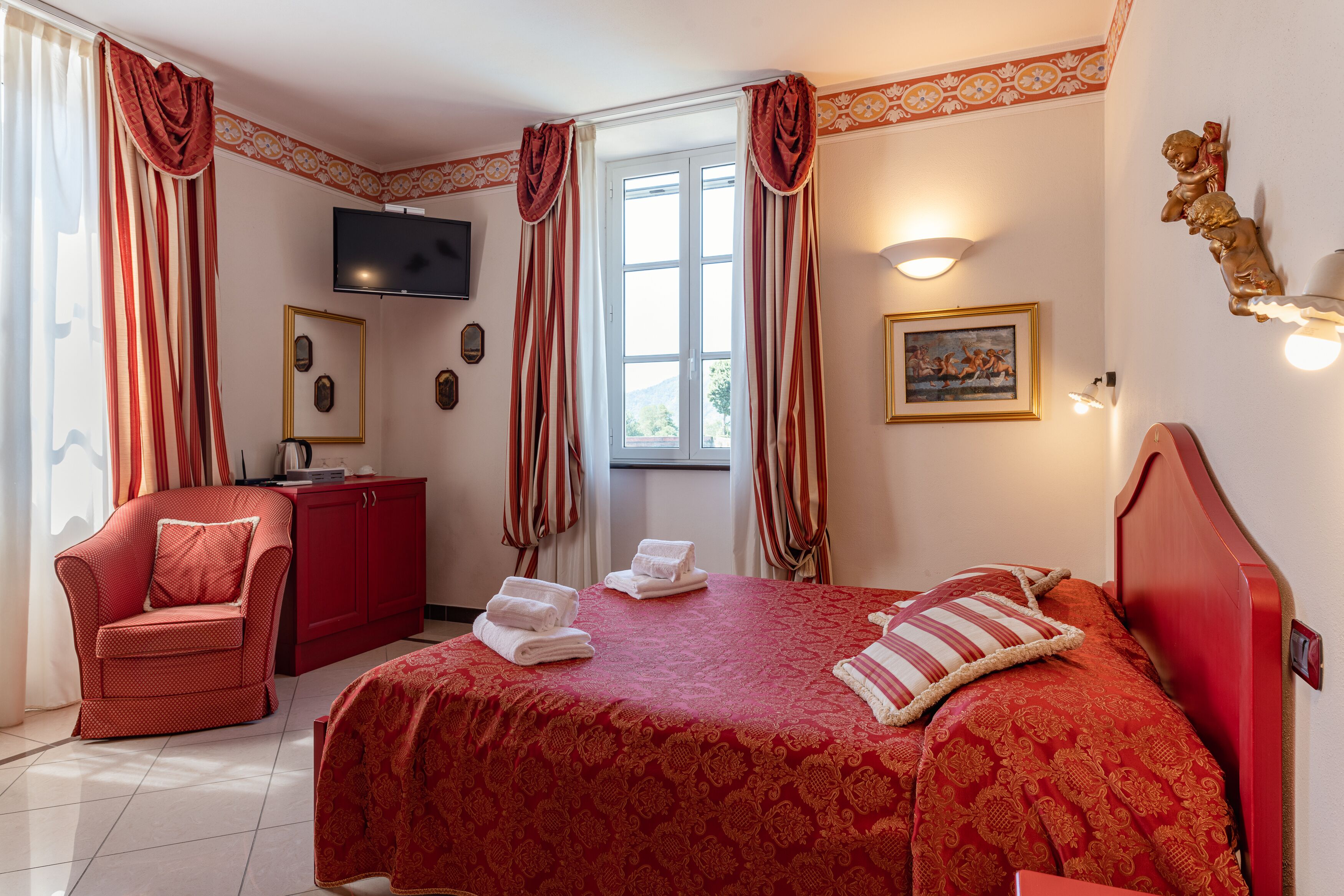 A hotel room with a bed, a red armchair, a television, and a window with curtains.