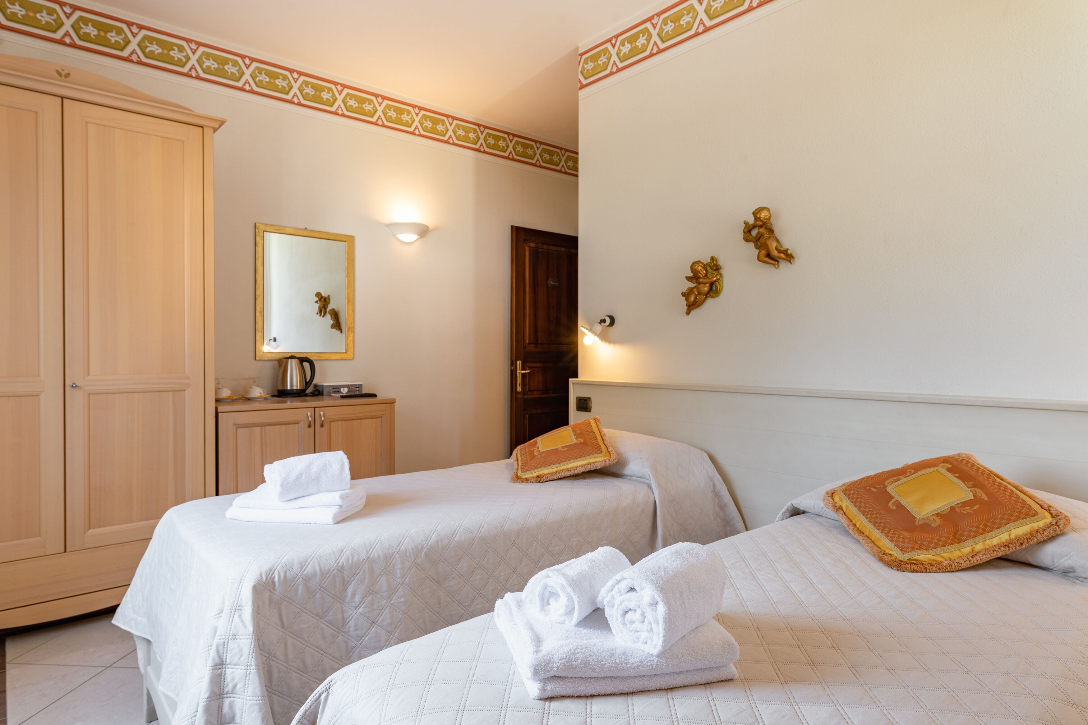 A hotel room with two beds, a wardrobe, a mirror, and decorative wall elements.