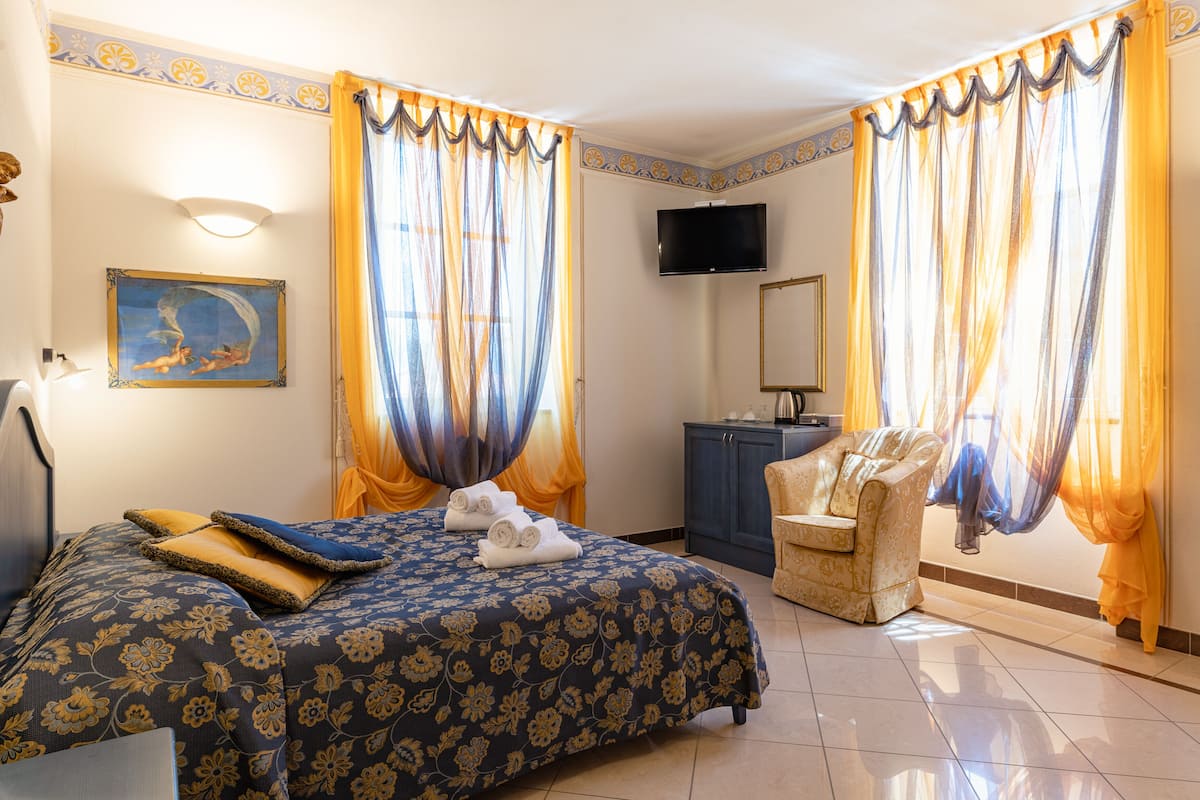 Una habitación de hotel con cama, una silla, un televisor y cortinas.