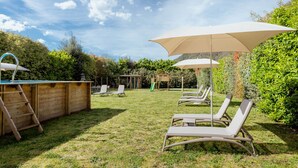 Un patio trasero con zona de barbacoa, sillas de descanso y una casita de juegos de madera.
