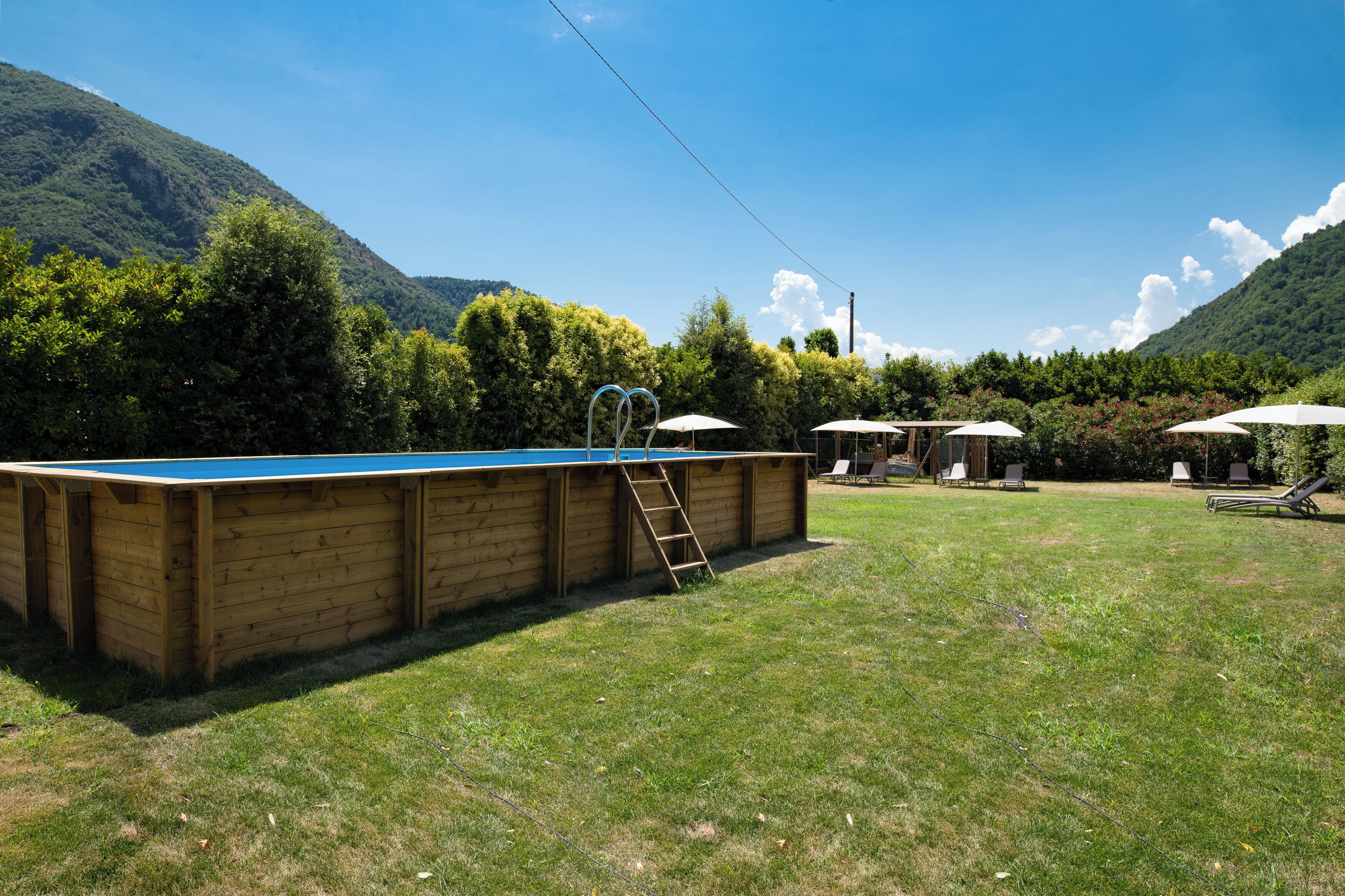 Ein Swimmingpool mit einer Holzterrasse, umgeben von einem Rasen mit Liegestühlen und Sonnenschirmen.