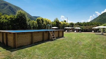Ein Swimmingpool mit einer Holzterrasse, umgeben von einem Rasen mit Liegestühlen und Sonnenschirmen.