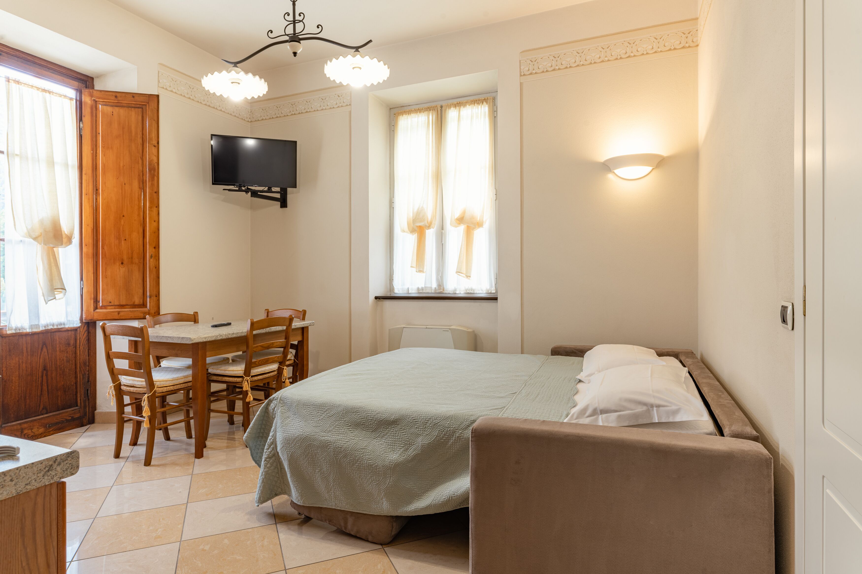 Un dormitorio con cama, escritorio, silla, televisor y ventana con cortinas.