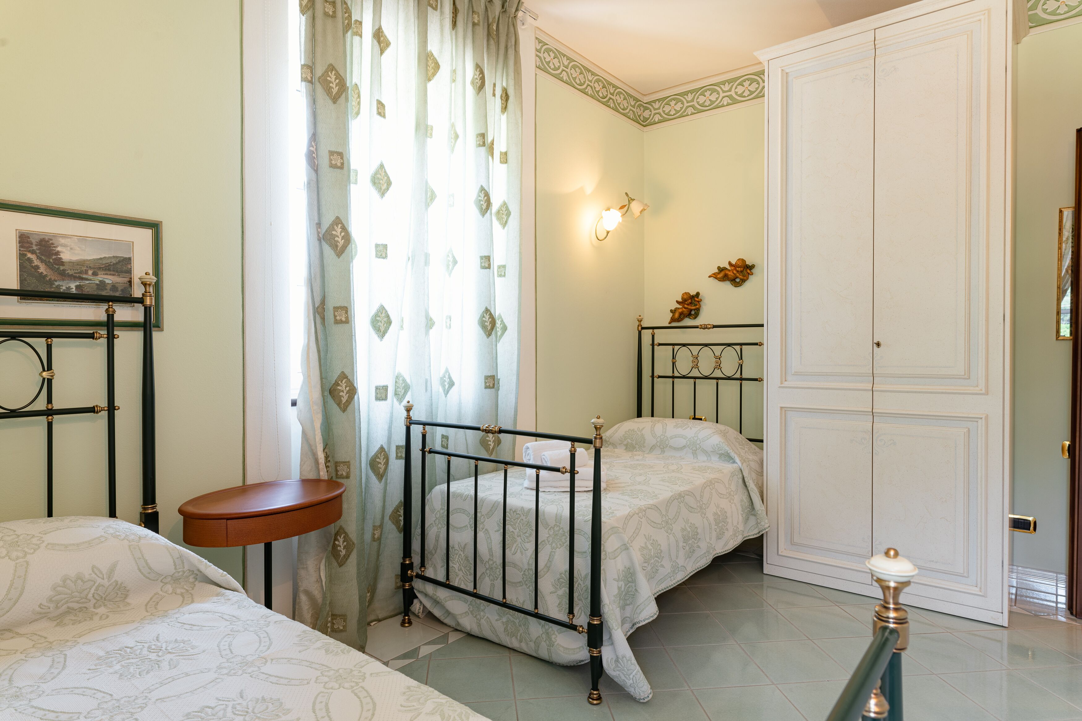 A bedroom with two beds, a bedside table, a wardrobe, and a wall-mounted light fixture.