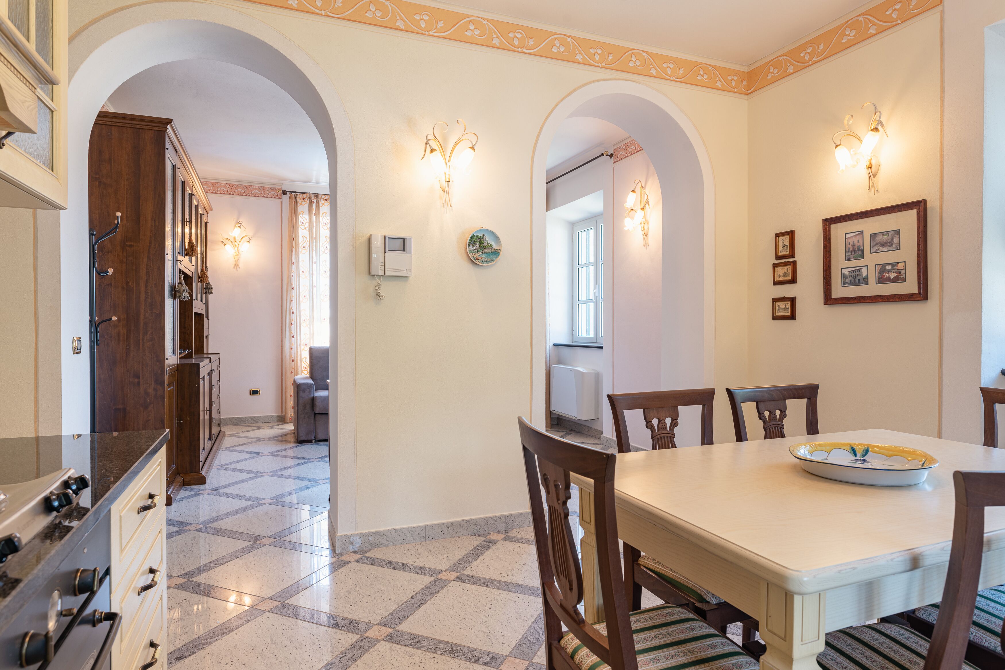 Un comedor con una mesa grande, sillas y un plato decorativo. Hay apliques de pared y cuadros enmarcados.