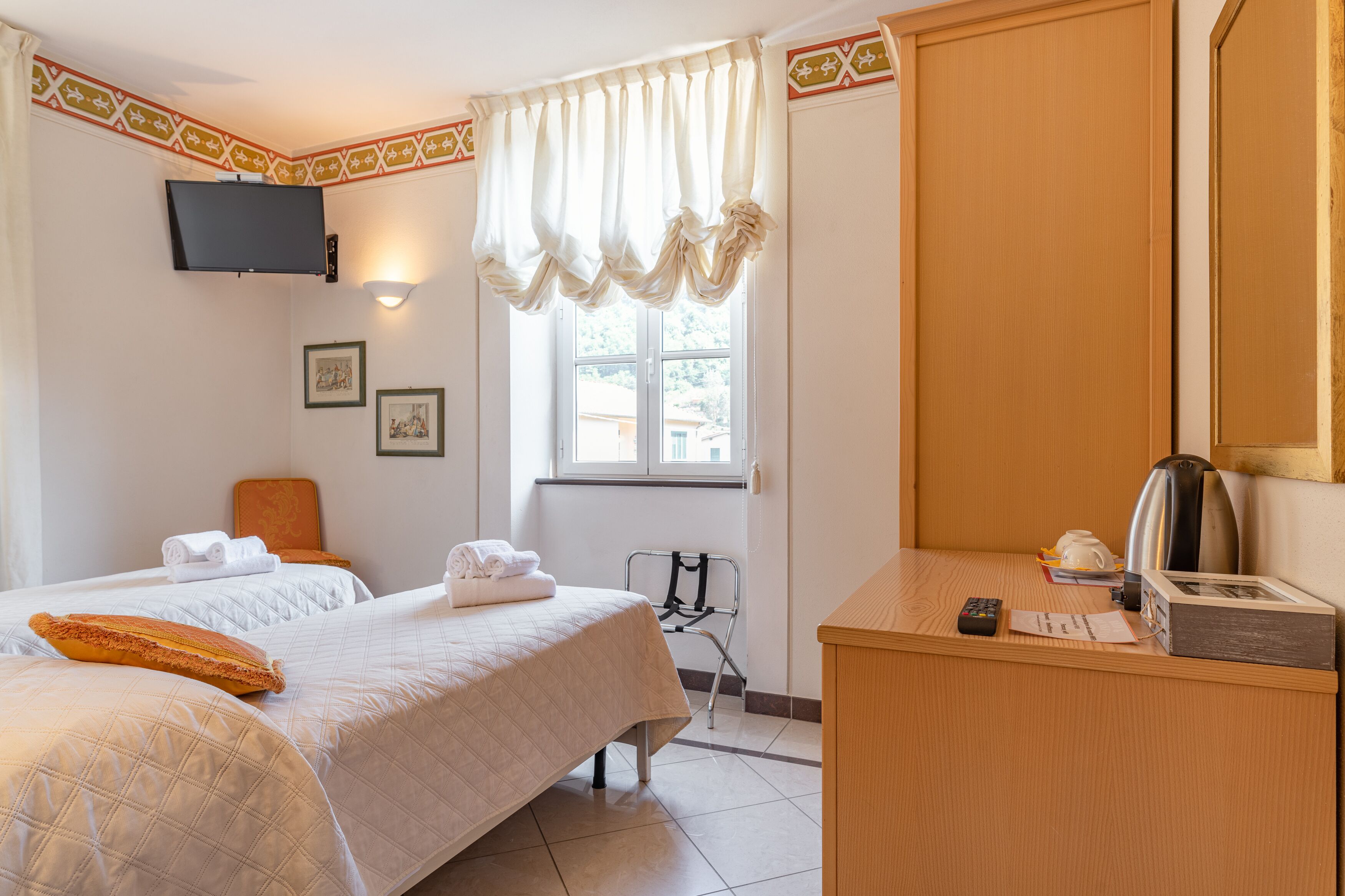 Habitación de hotel con dos camas, televisión, ventana con cortinas, escritorio con hervidor y una silla.