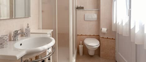 A bathroom with a sink, toilet, shower, and a mirror.